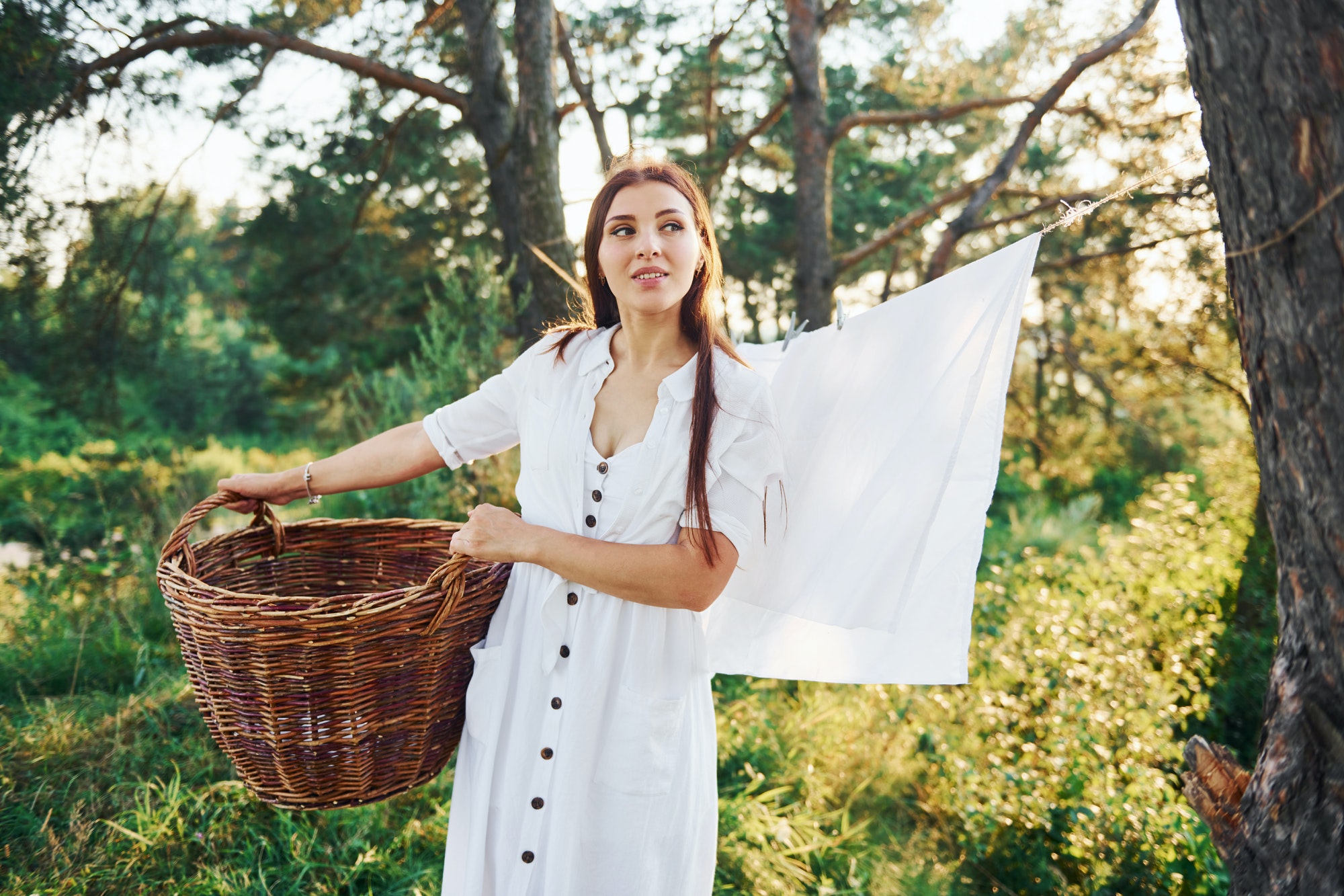 Young housewife with basket in hands hangs up washed clean white cloth to dry